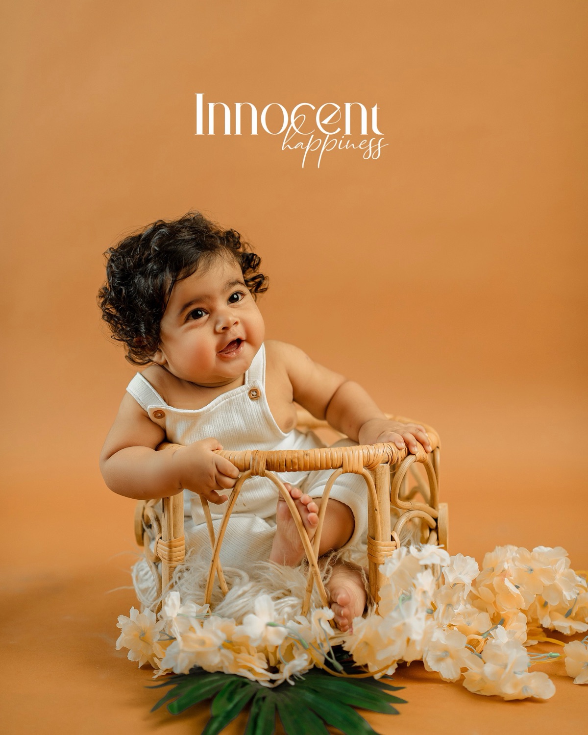 Baby smiling in a rattan basket with cream flowers on an amber backdrop