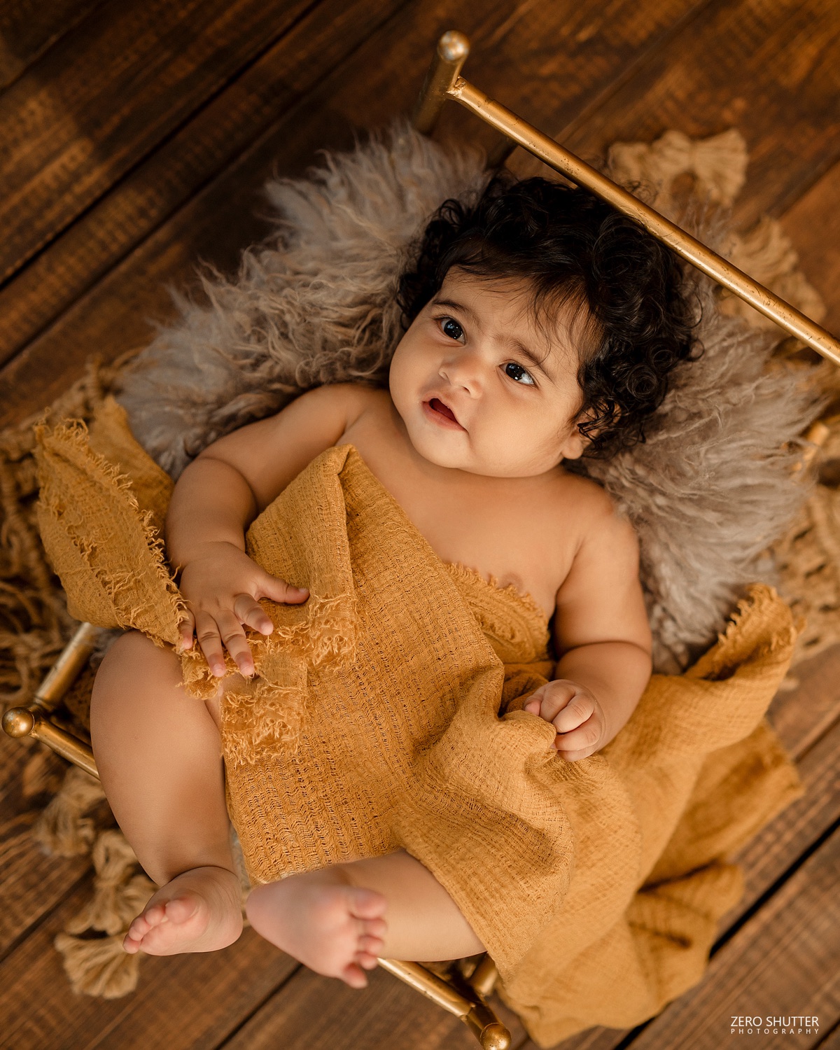 Baby wrapped in mustard cloth on a gold bed
