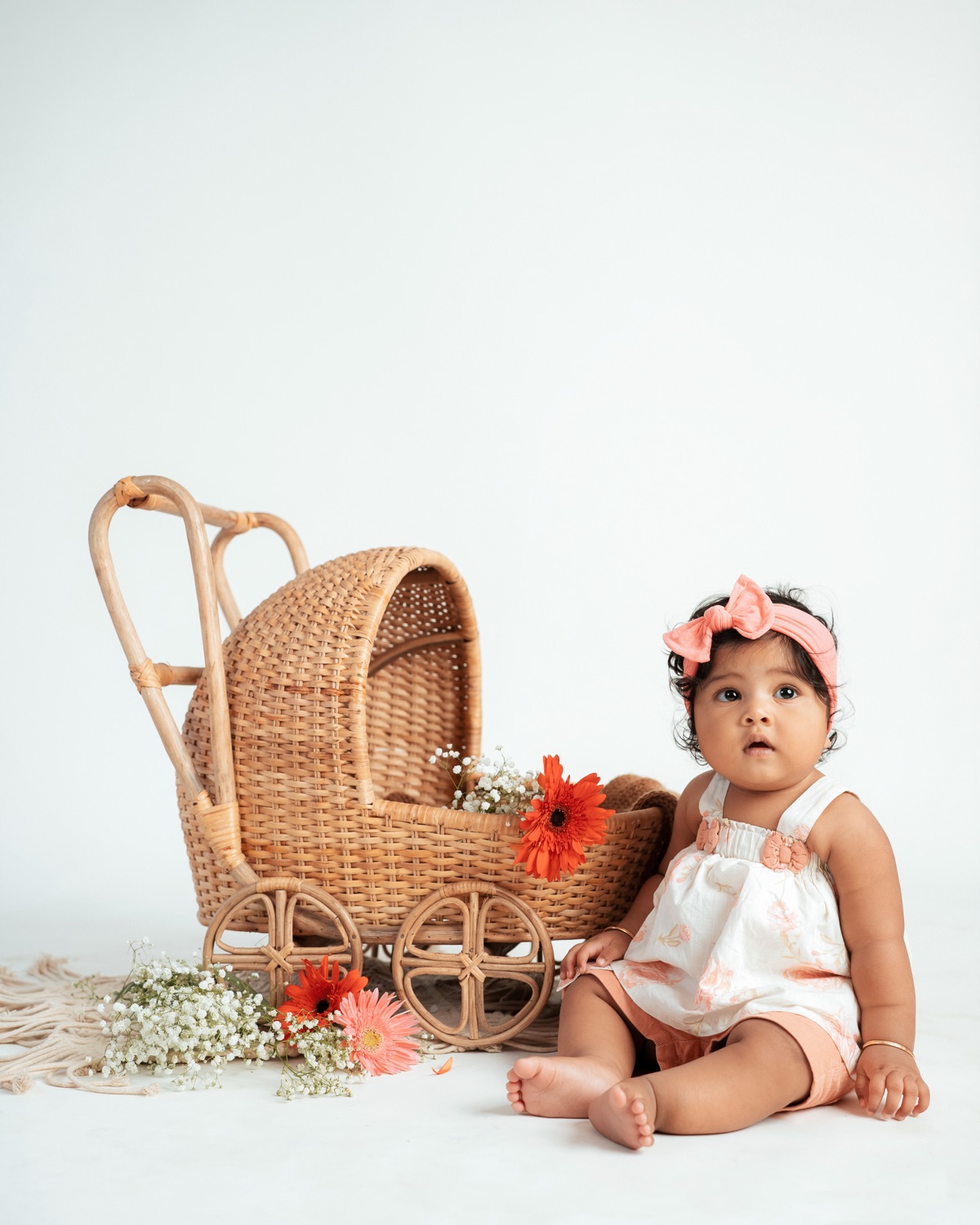 Baby seated beside a cane pram with flowers