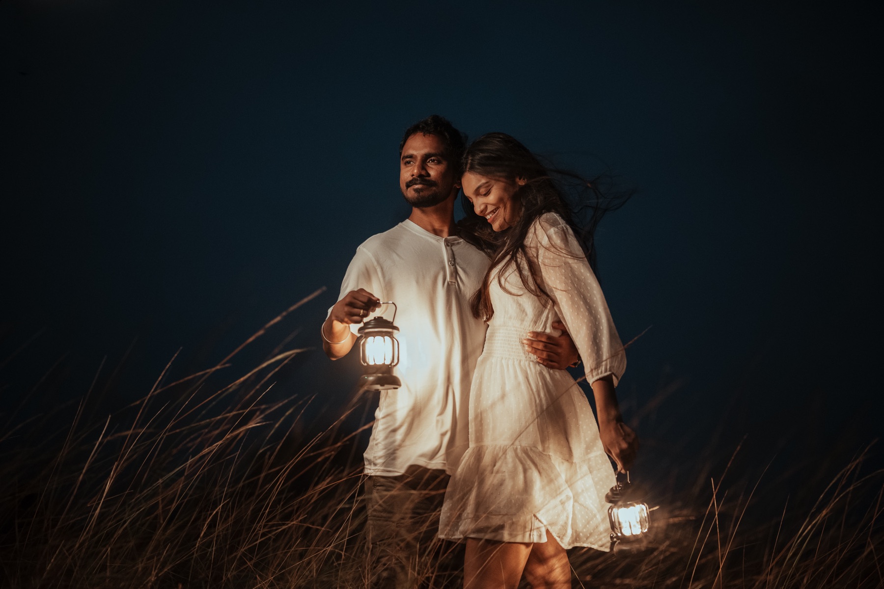 Couple holding lanterns in a field at dusk