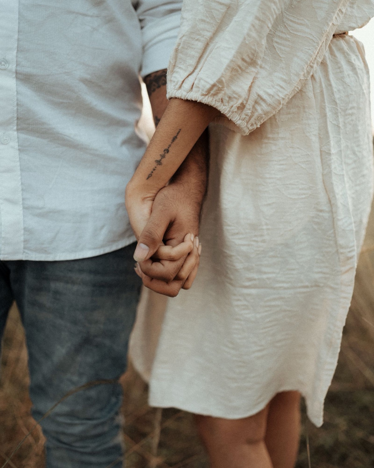 Couple holding hands in a field, her tattoo catching the light