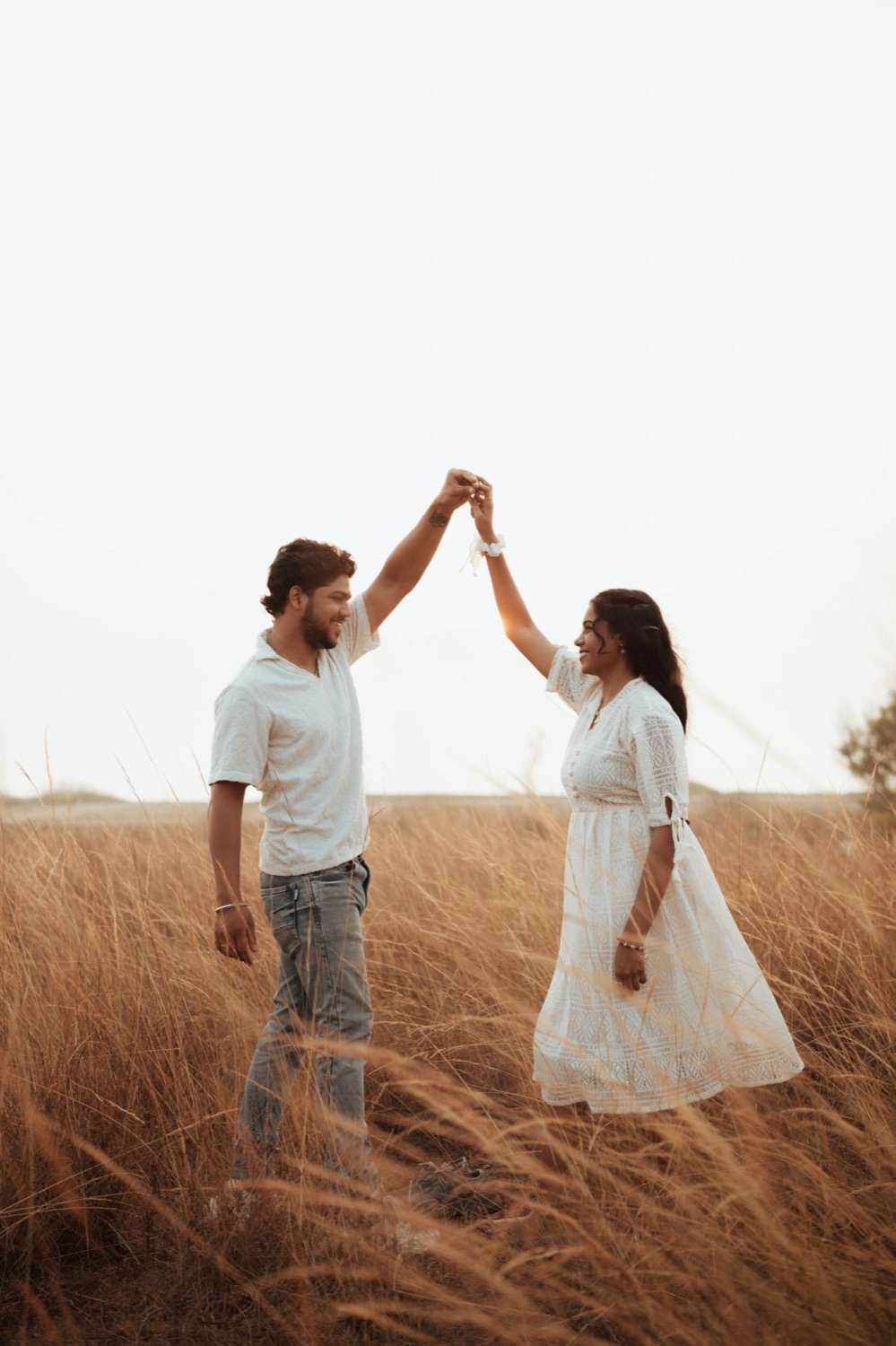 Couple dancing in tall golden grass, hands raised