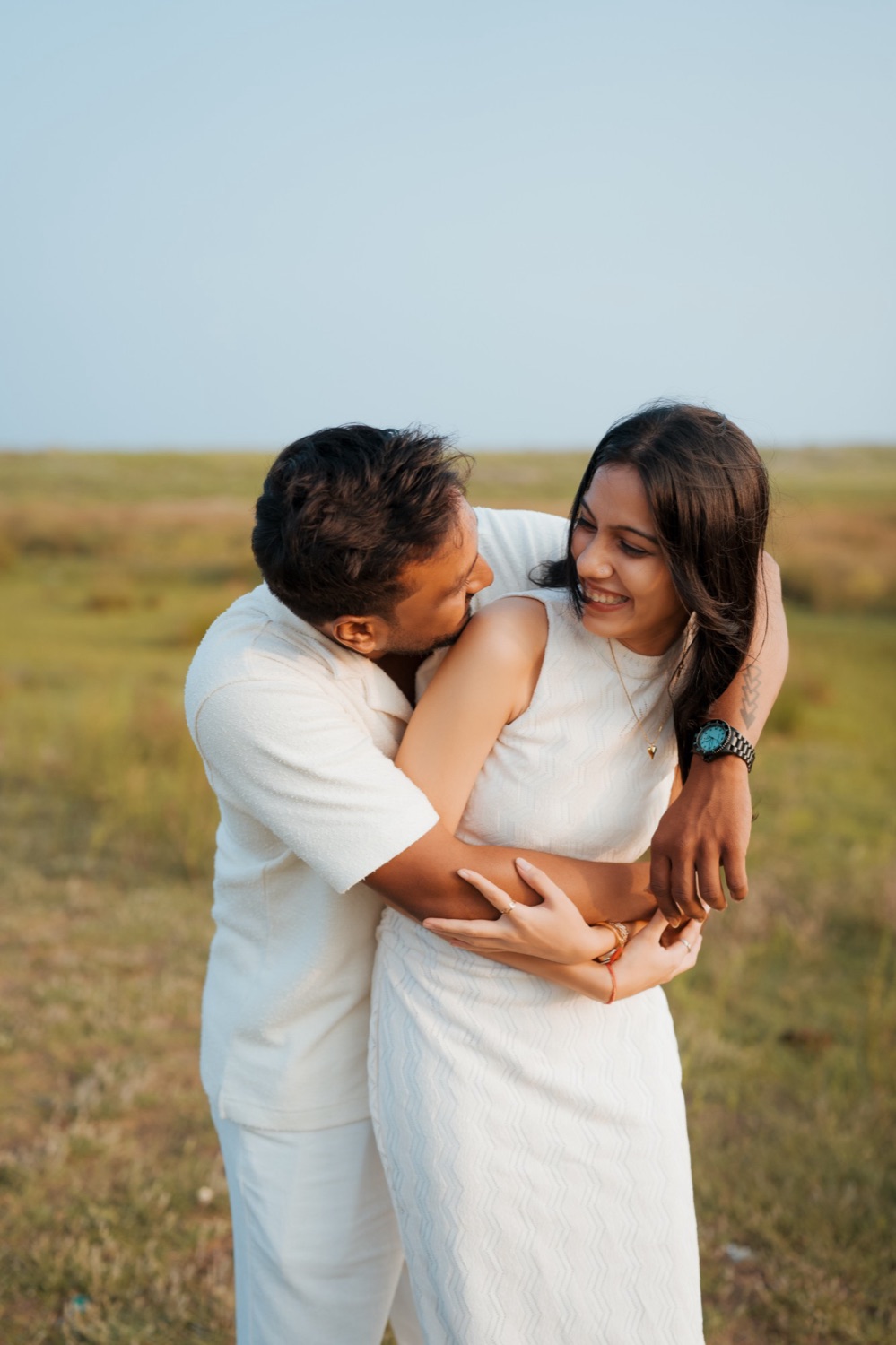 Couple laughing as he hugs her from behind in a green field