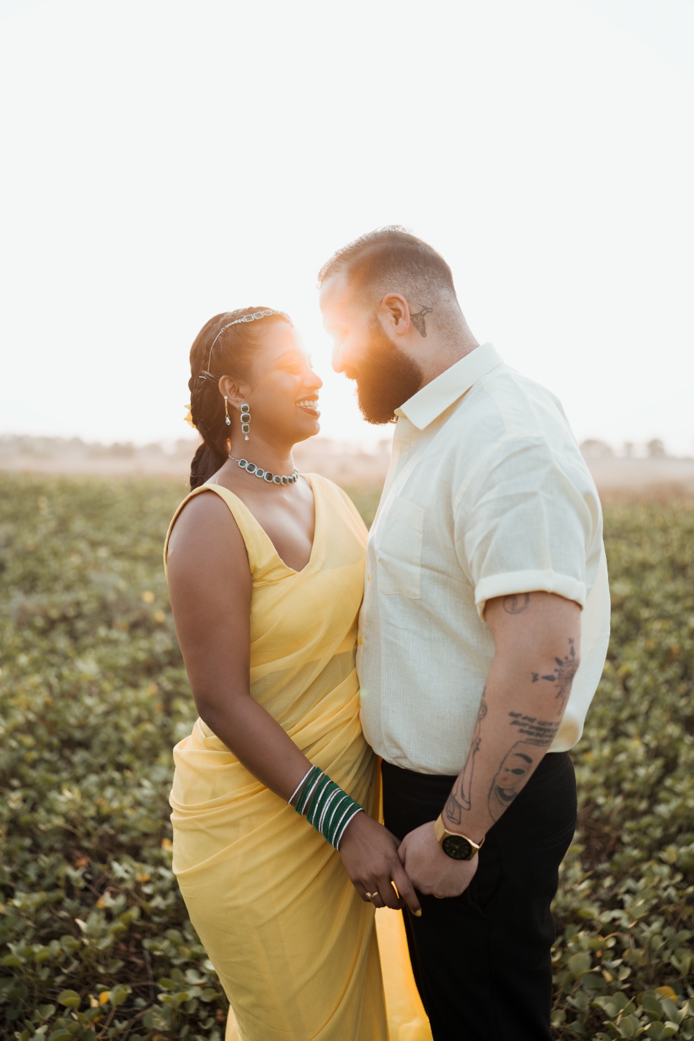 Couple in a field at golden hour, sun flaring behind them