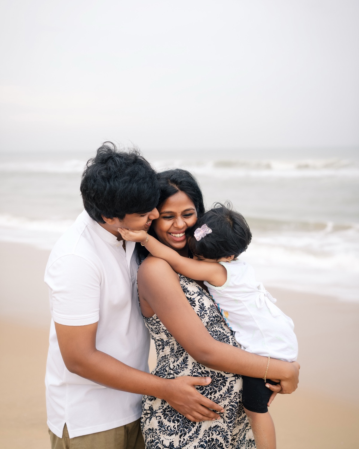 Family embracing on the beach as their toddler reaches for her mother