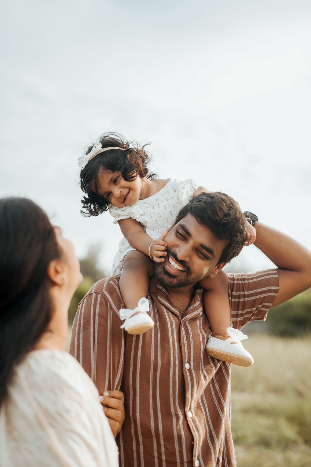Toddler on her father's shoulders as her mother looks up laughing