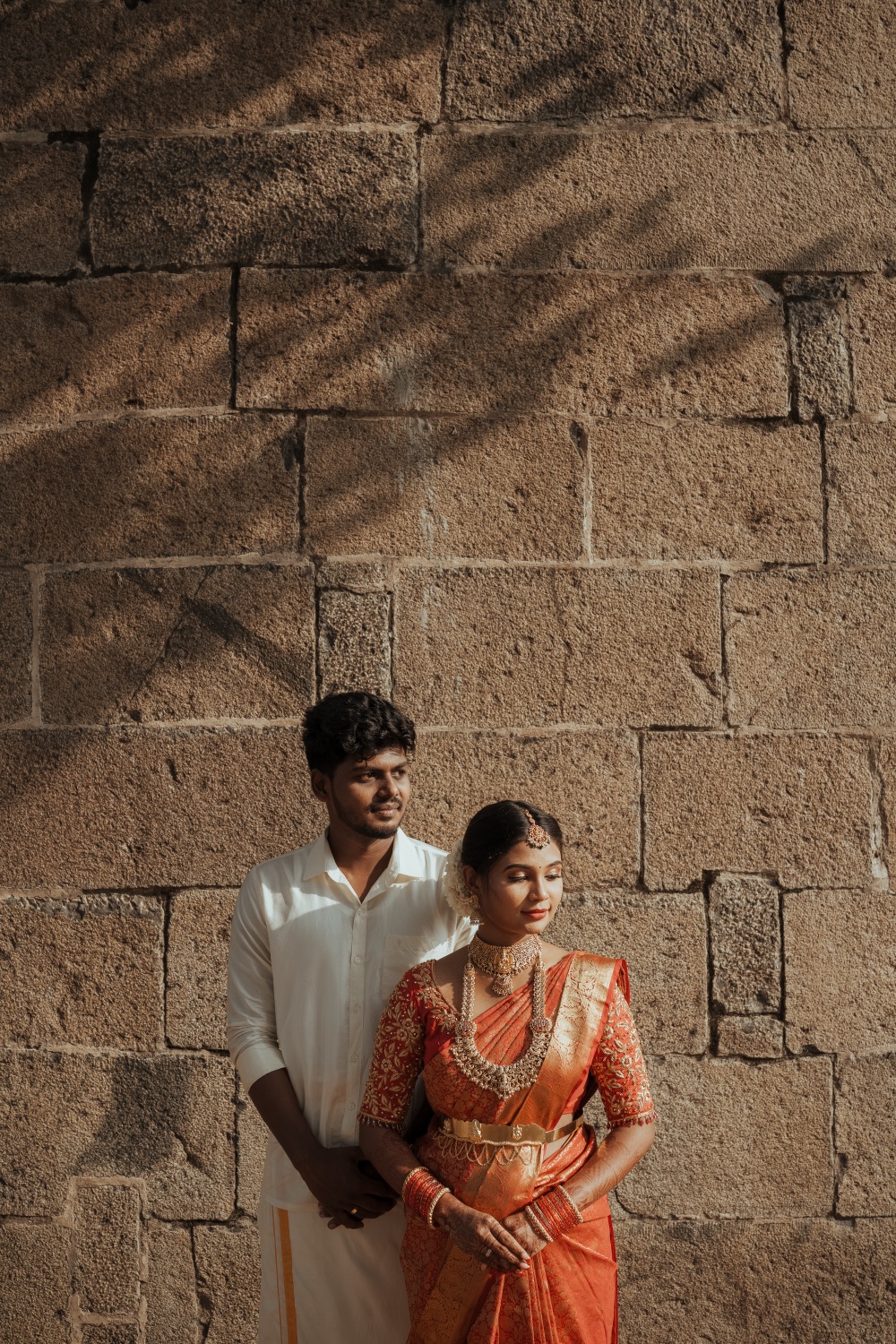 Bride and groom against a sunlit stone wall